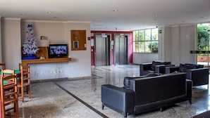 A lobby with a reception desk, a Christmas tree, seating area, and elevators. - Temporada Thermas Place Suítes Caldas Novas (Caldas Novas)