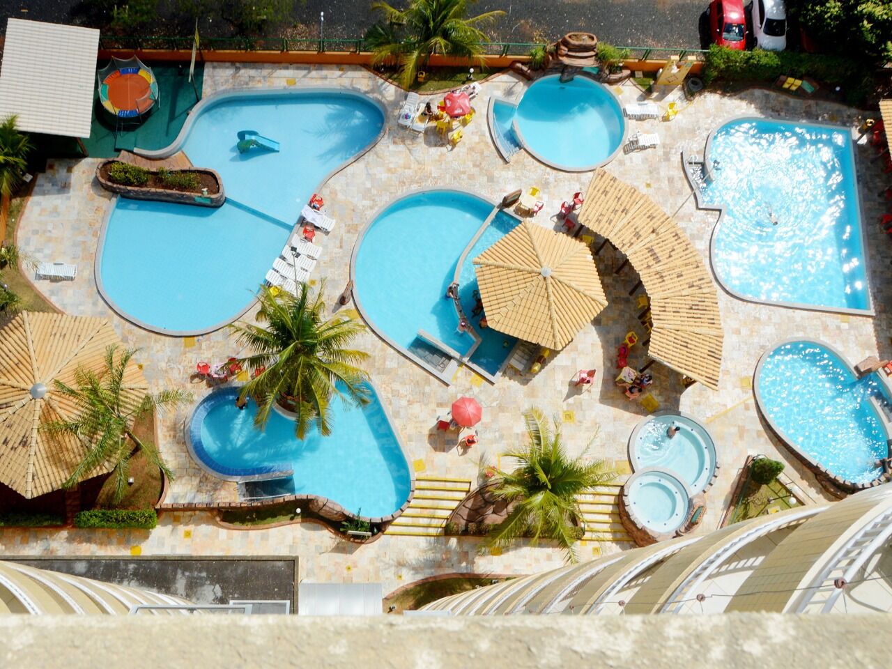 Eine Vogelperspektive eines Resorts mit mehreren Schwimmbecken, Liegestühlen, Sonnenschirmen und Palmen.