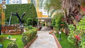 A pathway leading to a building with a covered entrance, surrounded by lush greenery and a decorative sculpture. - Temporada Thermas Place Suítes Caldas Novas (Caldas Novas)