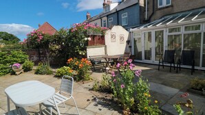 A patio with a table and chairs, surrounded by a garden with various flowers and plants. - The Old Police House (Saltburn-by-the-Sea)