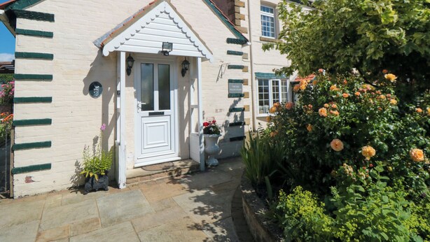 A quaint building with a white facade, a pitched roof, and a small porch with a white door. - The Old Police House (Saltburn-by-the-Sea)