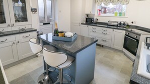A modern kitchen with white cabinets, a blue island, two bar stools, a microwave, a toaster, and an oven. - The Old Police House (Saltburn-by-the-Sea)
