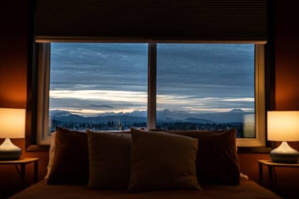 Enjoy breathtaking views of the surrounding mountains from the comfort of this room, featuring a bed and two bedside tables with lamps.