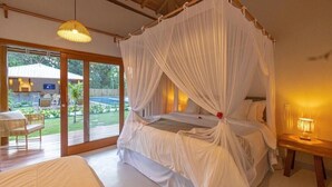 A bedroom with a canopy bed, a small table with a lamp, and a view of a pool and outdoor seating area.