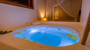 A large, oval-shaped hot tub with a blue interior, surrounded by beige walls and a window with curtains.