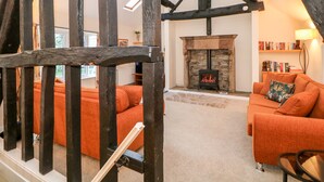A cozy living room with a stone fireplace, wooden beams, and orange furniture. - Wilson Eyre Cottage (Hope Valley)