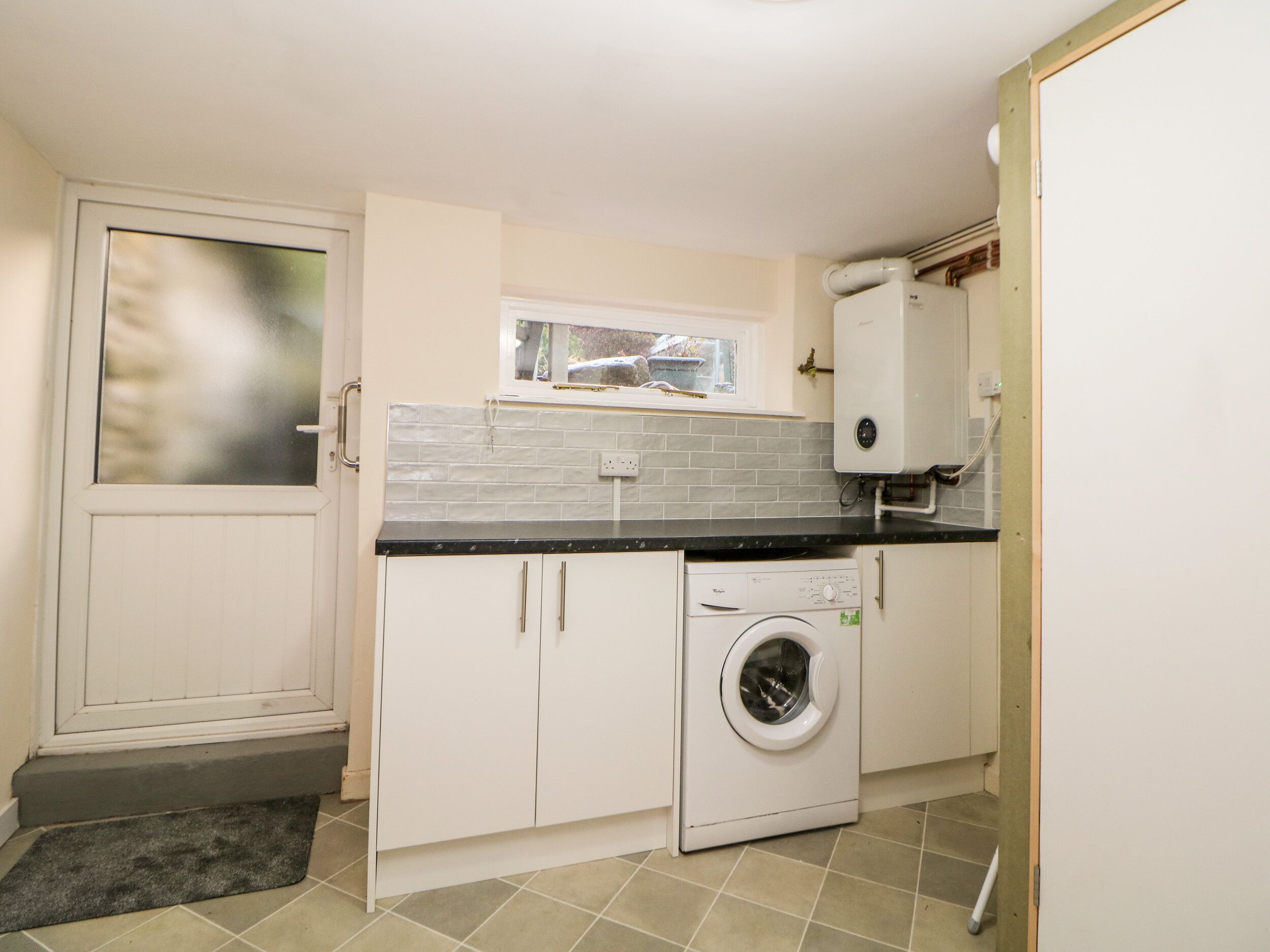 A compact kitchen with a built-in washer and dryer, a window above the sink, and a door with a frosted glass panel.