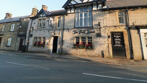 A traditional stone building with a black and white timber-framed upper story, a signboard, and flower boxes. - Wilson Eyre Cottage (Hope Valley)