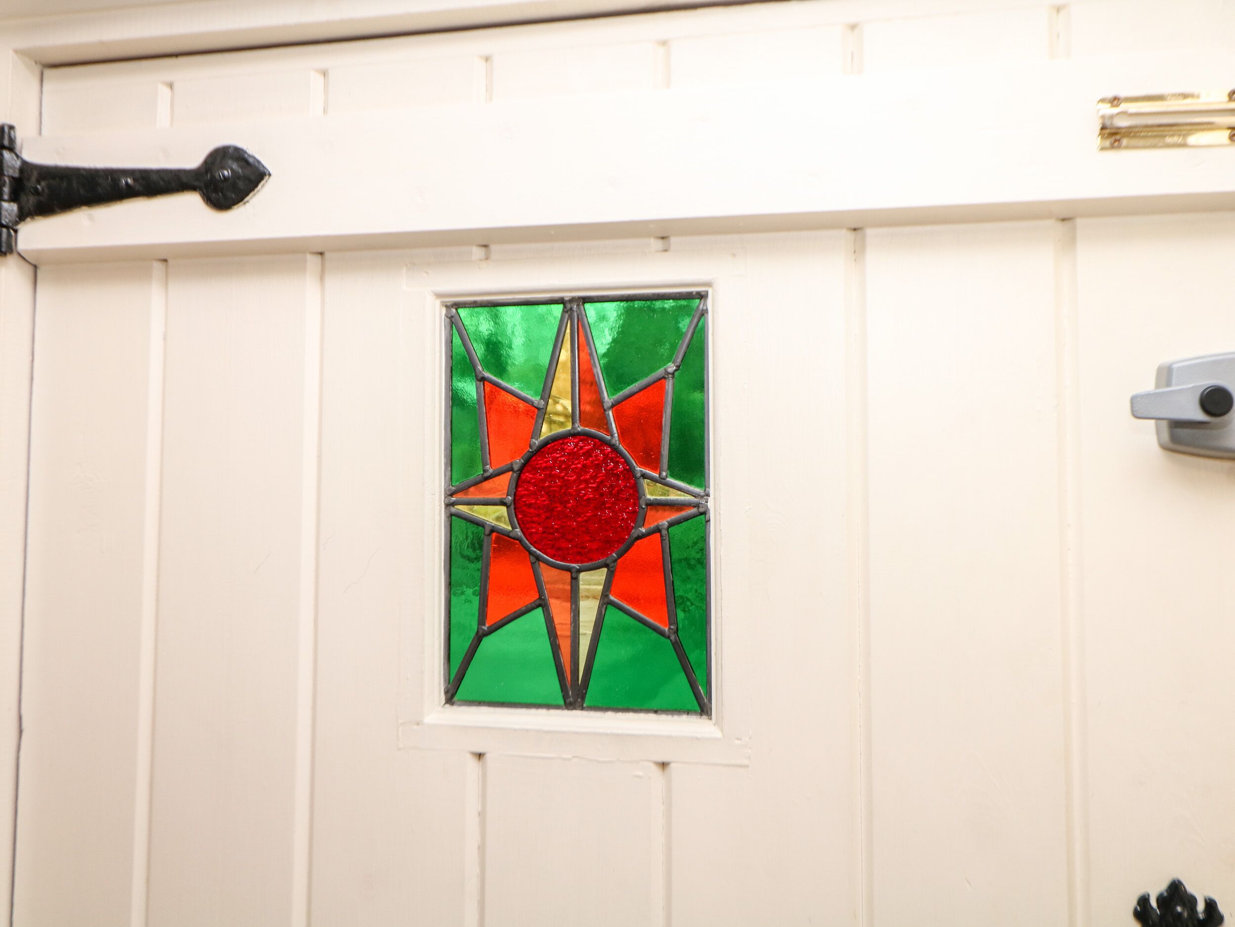 A white door with a stained glass window featuring a red center and green and orange patterns.