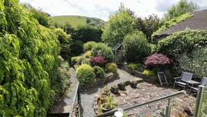 A garden with a stone pathway, potted plants, and outdoor seating. - Wilson Eyre Cottage (Hope Valley)