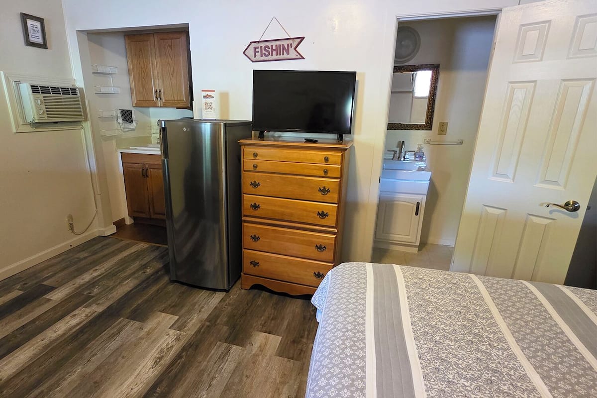A compact room with a bed, a dresser, a refrigerator, a television, and a small kitchenette.