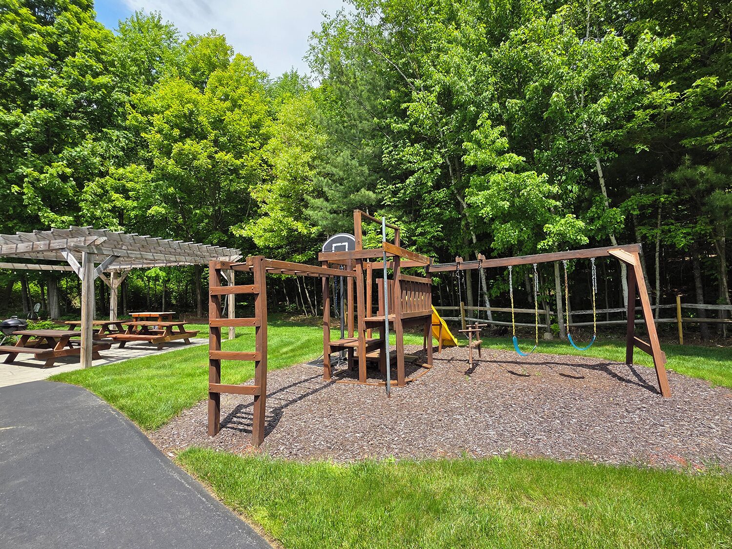 Un parque infantil con una estructura de madera para escalar, columpios y un tobogán.