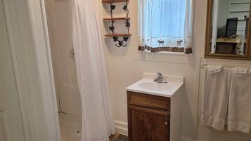 A bathroom with a shower, a sink, a mirror, and a window with curtains.