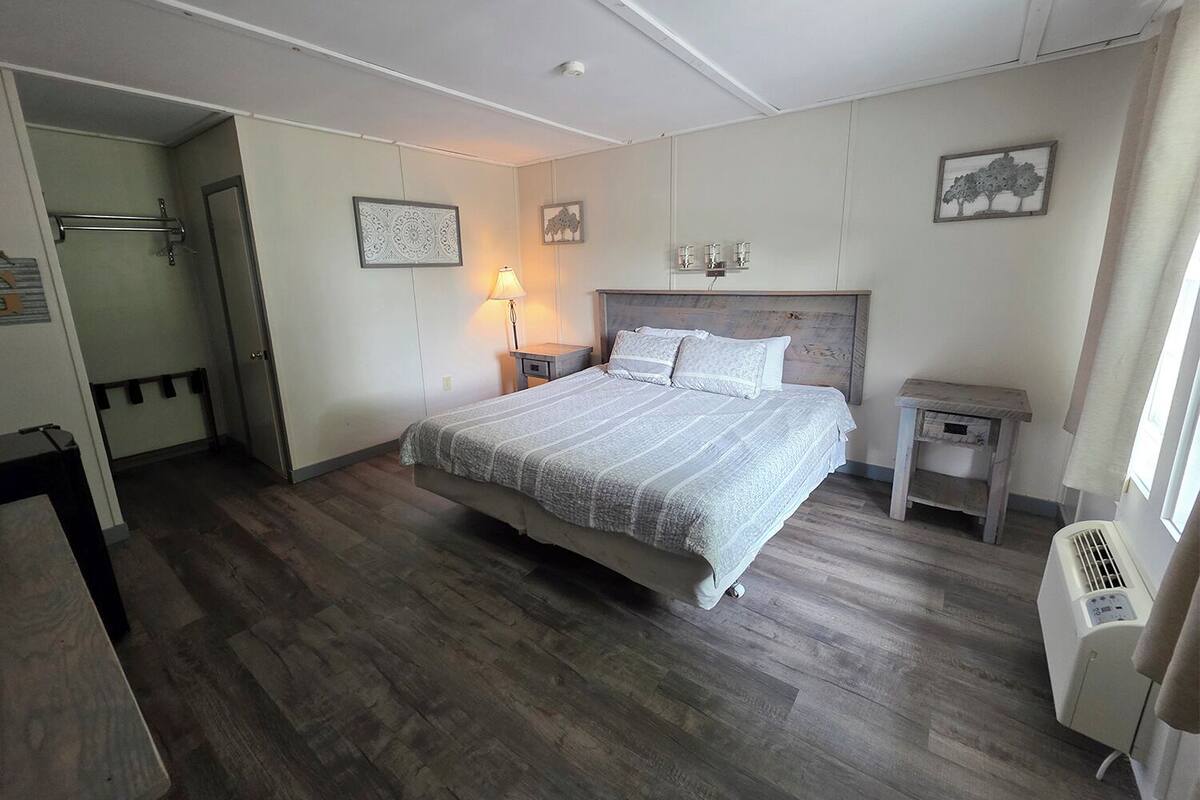 A bedroom with a bed, bedside tables, a lamp, a heater, and a door leading to another room.