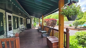 A covered outdoor deck with wooden furniture and a hanging planter. - Adirondack Sunrise Motel and Cabins (Lake George)