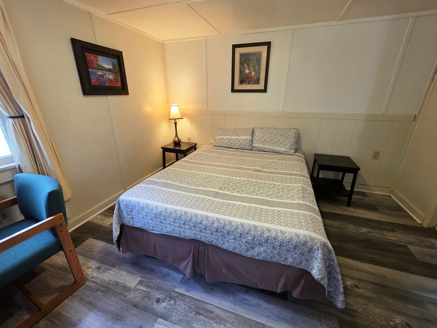 A bedroom with a bed, a nightstand, a lamp, a chair, and two framed pictures on the wall.