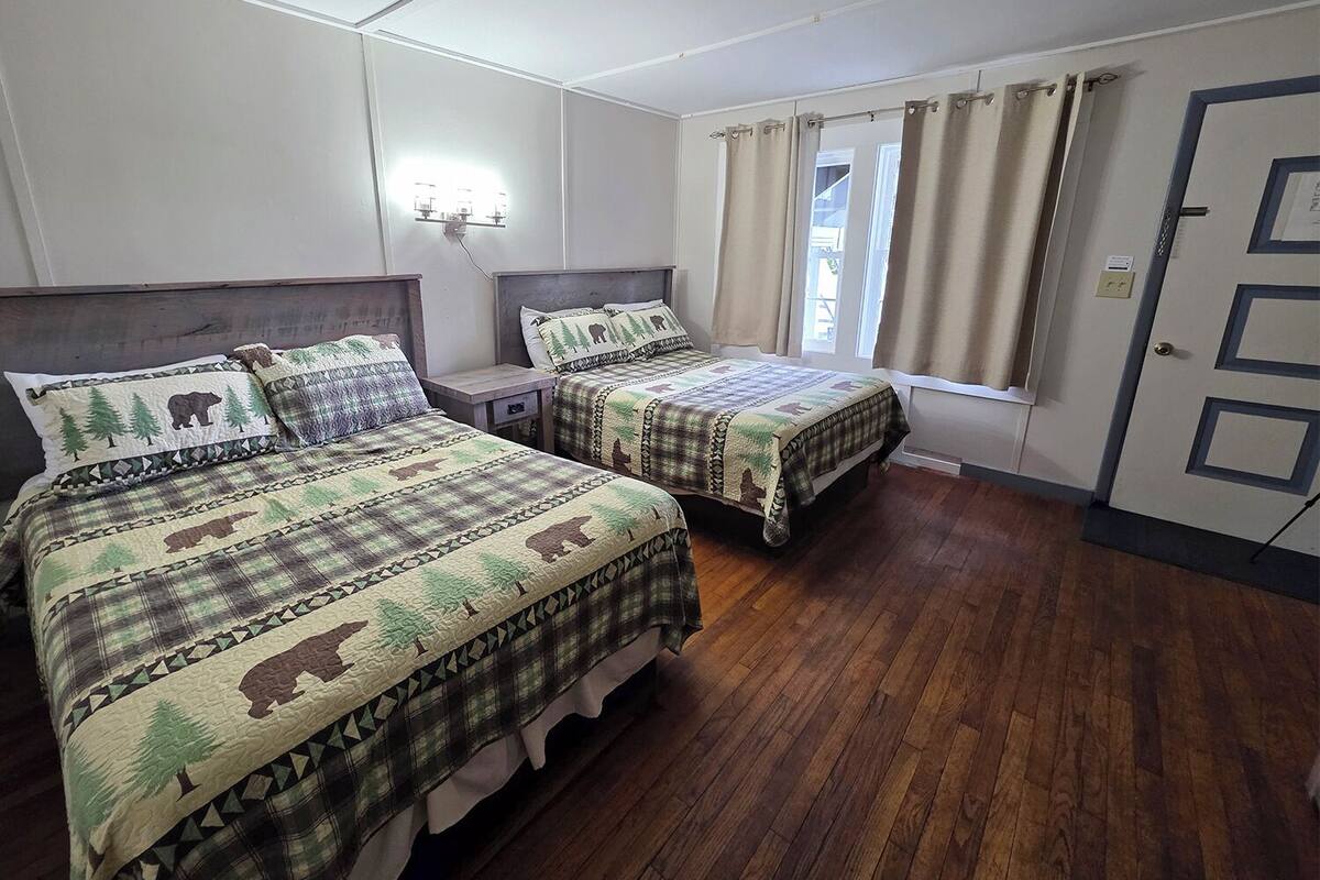 A bedroom with two beds, wooden flooring, a window with curtains, and a door with a lock.