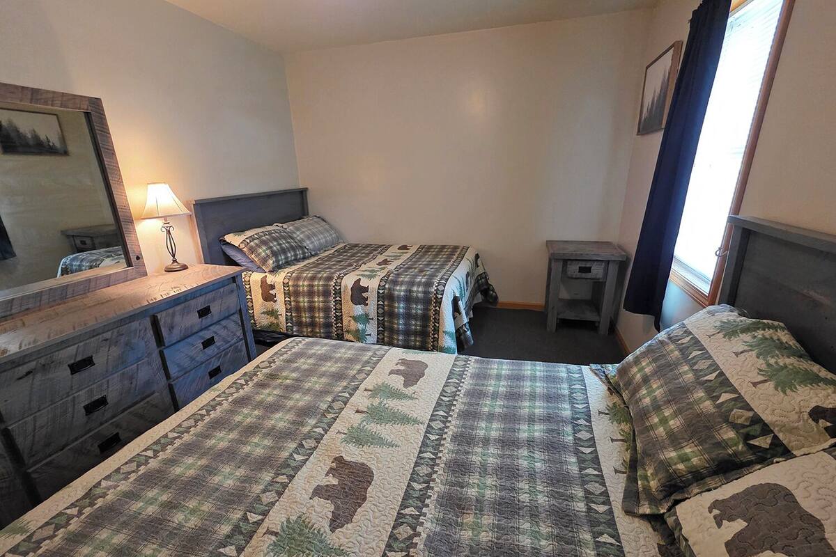 A bedroom with two beds, a dresser, a nightstand, a lamp, and a window with curtains.
