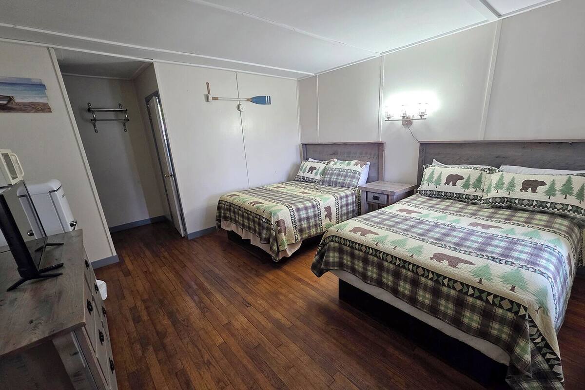 A bedroom with two beds, wooden flooring, a wardrobe, and a small table.