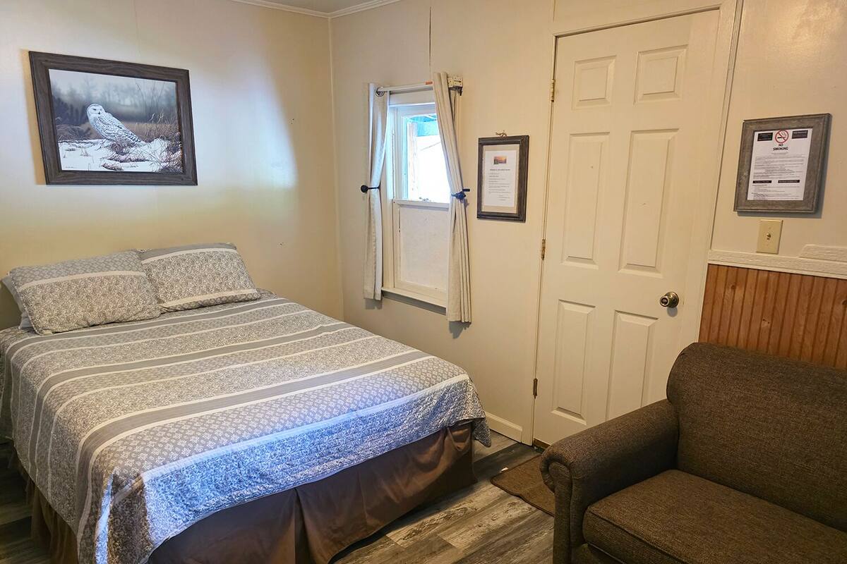 A bedroom with a bed, a chair, a window with curtains, and a door.