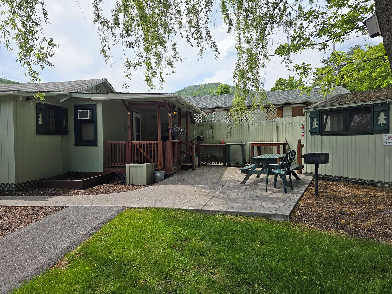 A small, fenced outdoor area with a picnic table and chairs, a barbecue grill, and a covered seating area.
