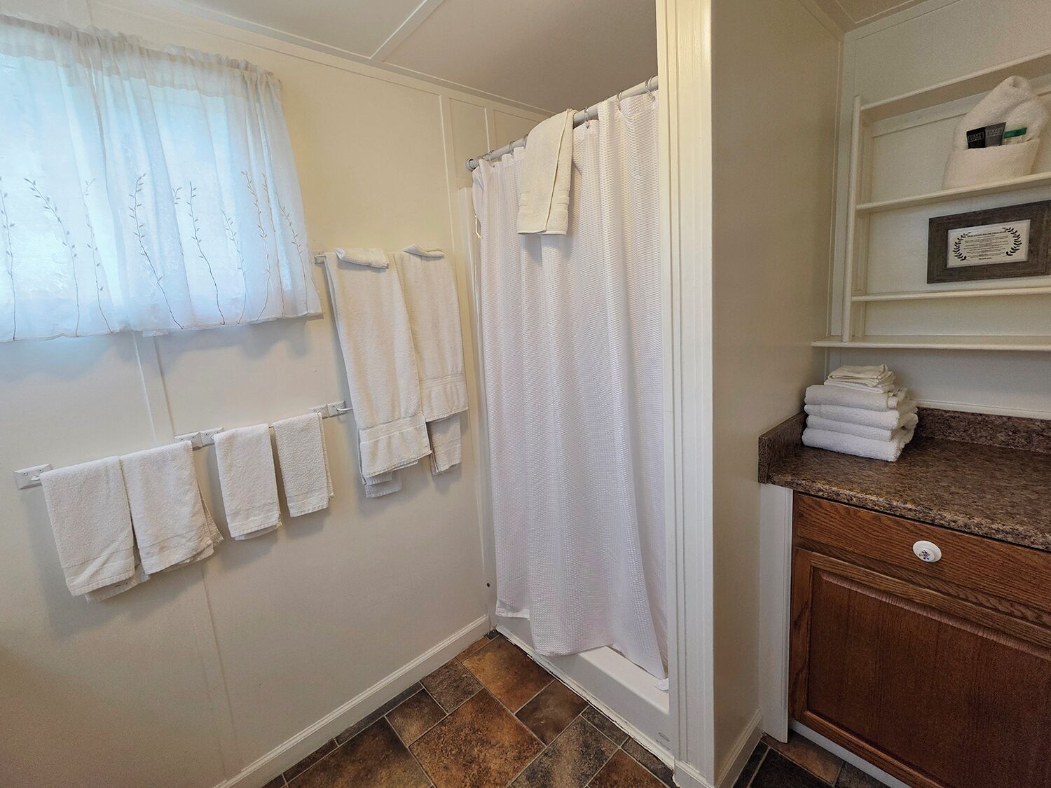 Une salle de bain avec un rideau de douche, plusieurs serviettes rangées sur un porte-serviettes et un meuble-lavabo en bois sur lequel sont pliées d’autres serviettes.