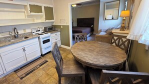 A compact kitchen with white cabinets, a stove, and a microwave. There's a dining area with a wooden table and chairs. - Adirondack Sunrise Motel and Cabins (Lake George)