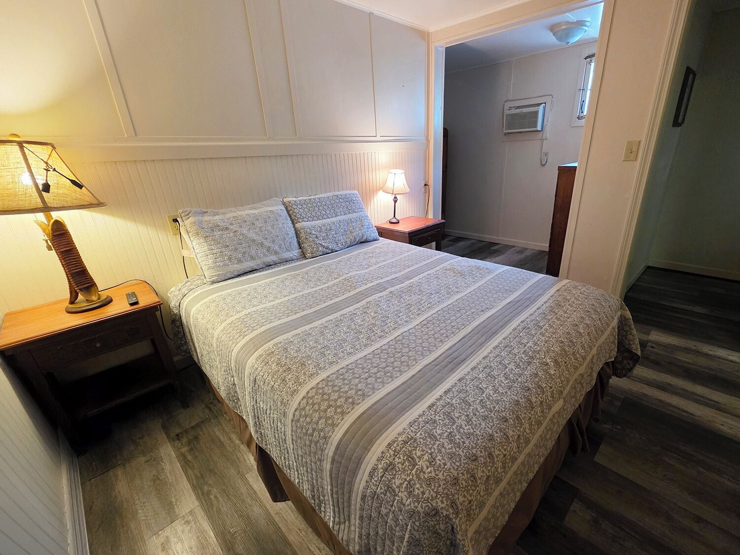 Un lit bien fait, recouvert d’une couvre-lit à motifs, avec deux lampes de chevet et une table de chevet en bois.