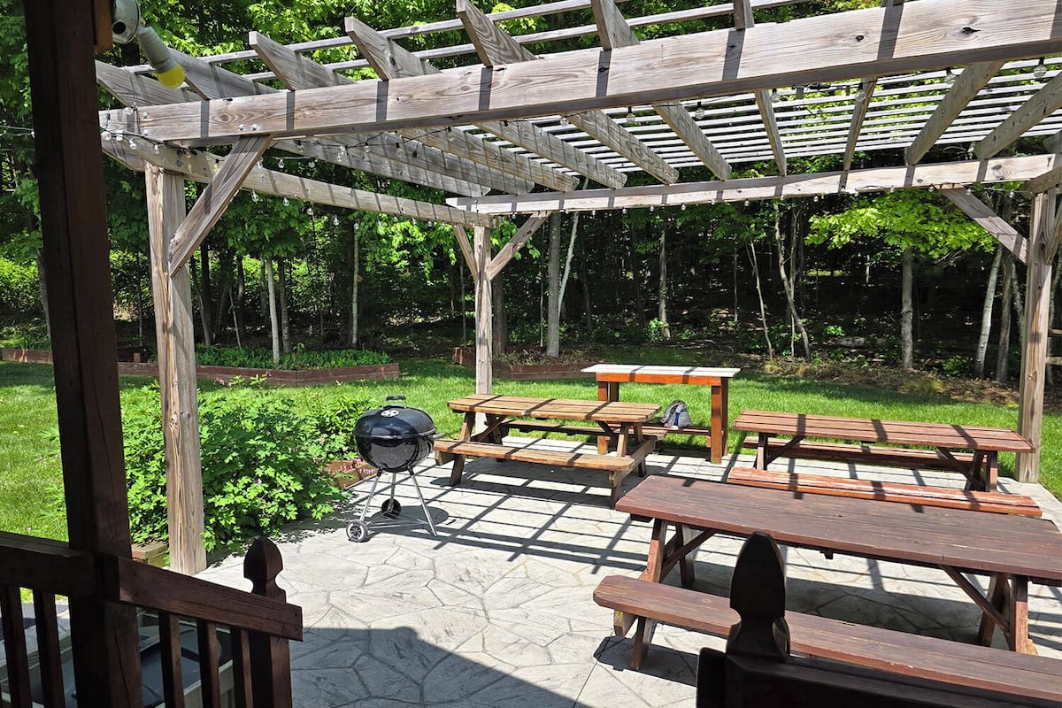 A wooden pergola with picnic tables and a barbecue grill.