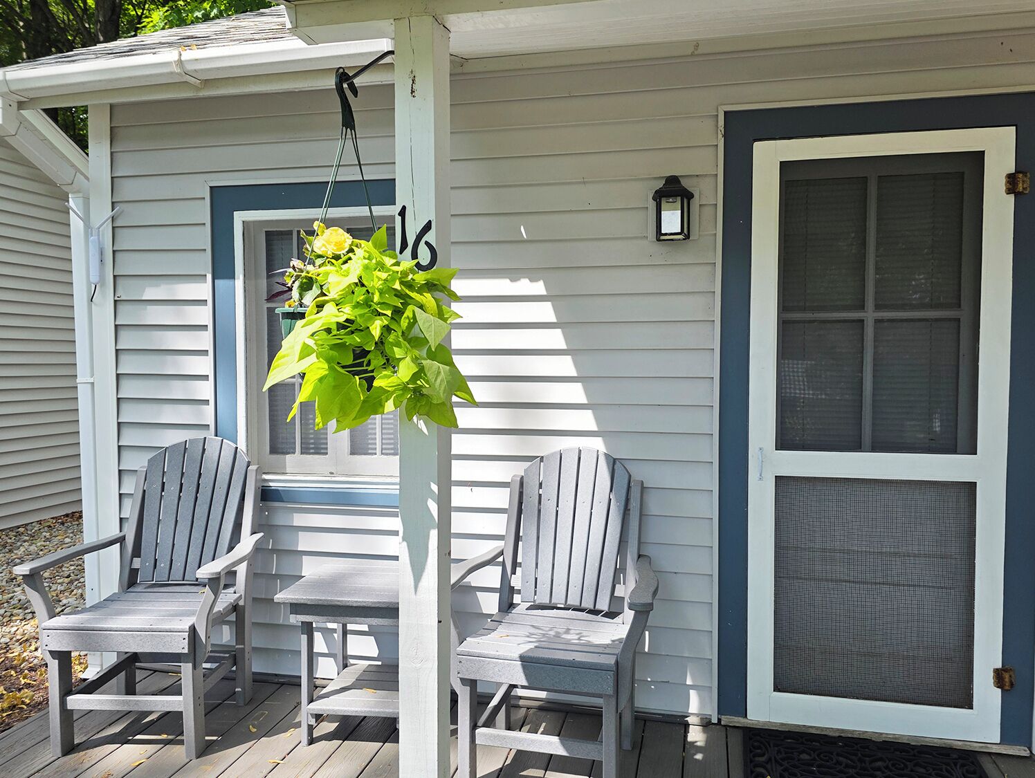 A porch with two Adirondack chairs and a hanging plant.
