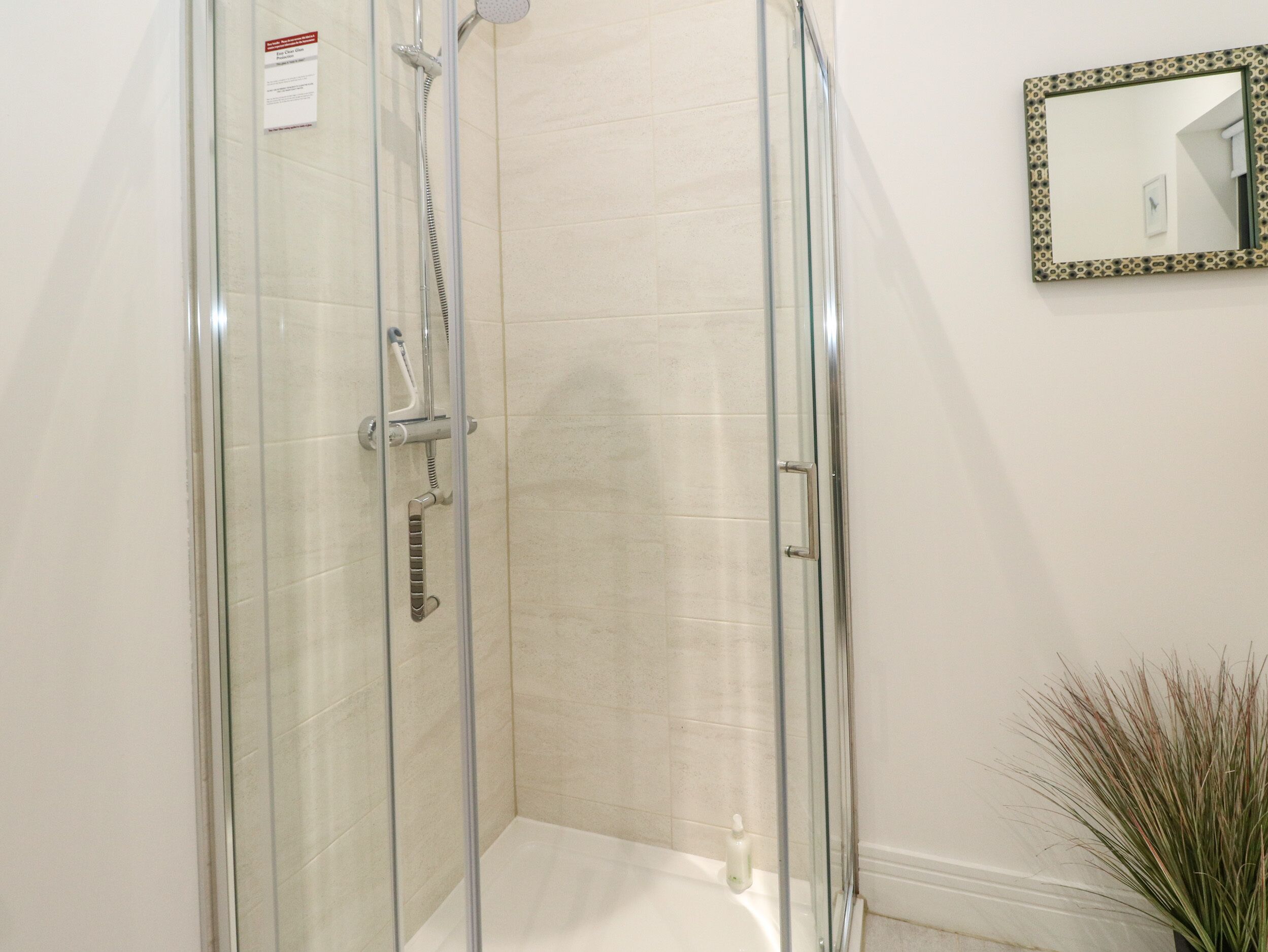 A glass-enclosed shower with a handheld showerhead and a handheld shower attachment.