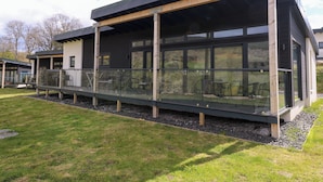 Un bâtiment moderne doté d’un espace extérieur couvert, de grandes fenêtres et d’une pelouse verdoyante.