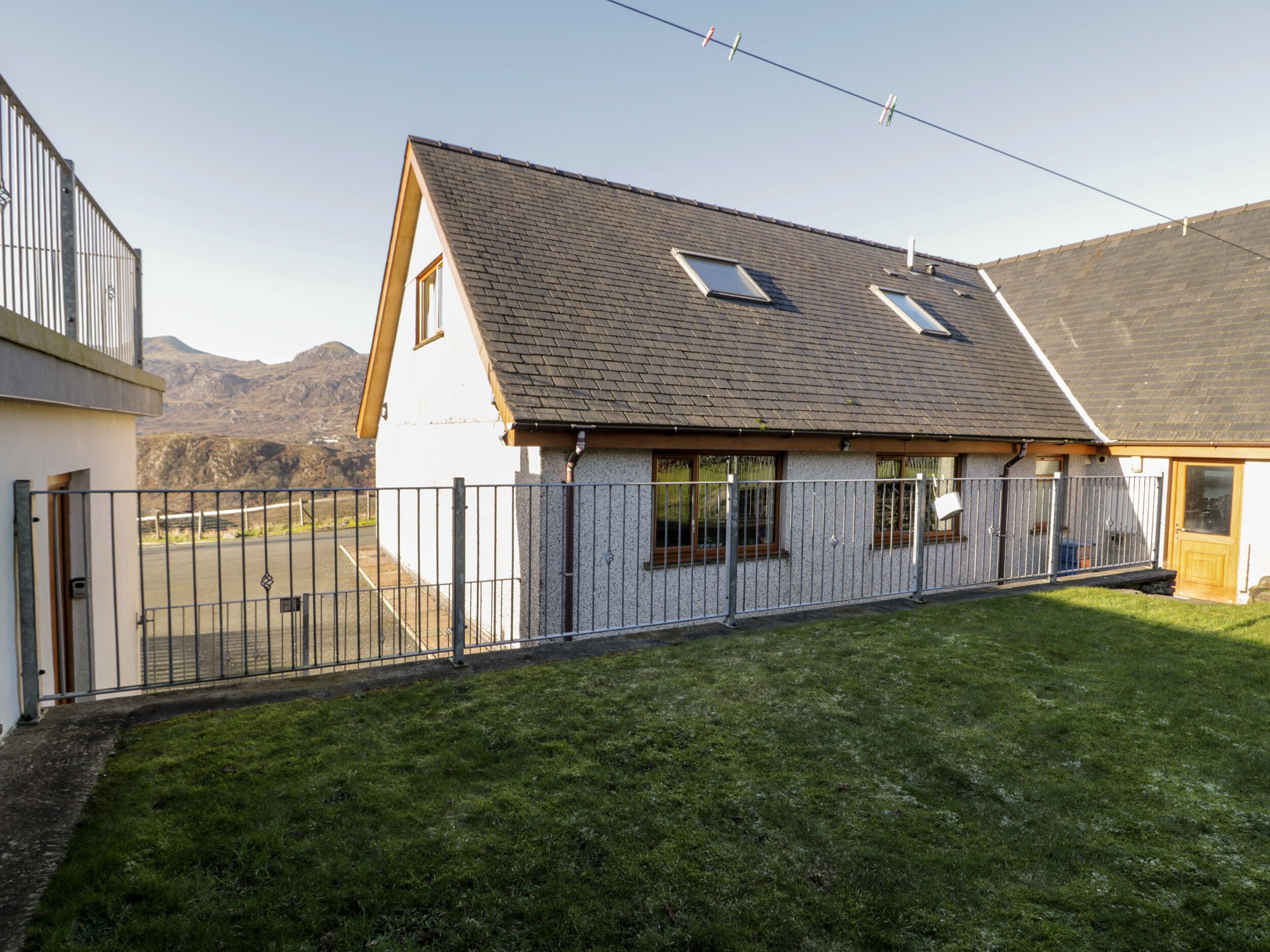 Een tweelaags huis met een schuin dak, een omheind erf en een berg op de achtergrond.