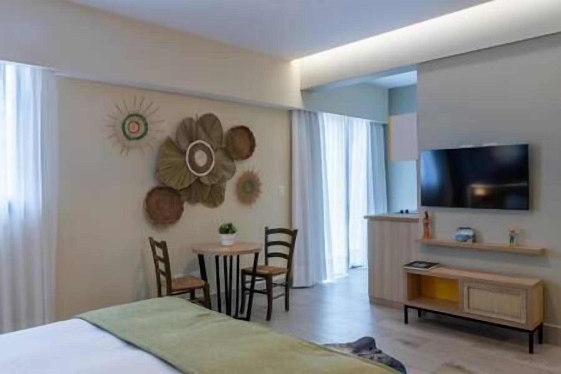 Una habitación de hotel moderna con cama, televisor, una pequeña mesa con sillas y decoración en la pared.