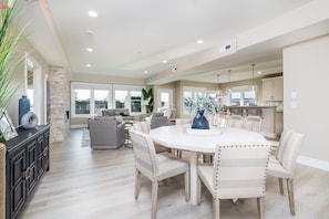 A spacious living room with a round dining table, light-colored chairs, and a fireplace.