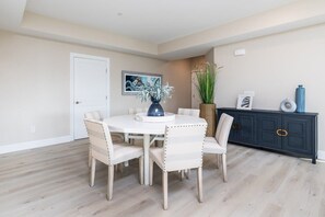 A dining area with a white table and chairs, a dark blue cabinet, and a painting on the wall. - Luxurious Bay/ Ocean view Splendor 4 BRS elevator (Ocean City)