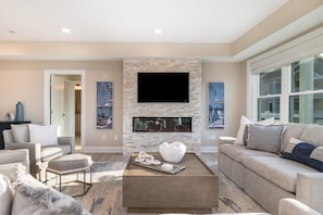 A modern living room with a stone fireplace, a flat-screen TV, and contemporary furniture.