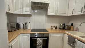 A kitchen with white cabinets, a microwave, a stove, and a washing machine. - Cosy 1bed in Wembley  (Wembley)