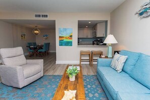 A living room with a sofa, armchair, coffee table, and a dining area with chairs and a table. - Oceanfront condo with pool, sleeps 4, free Wi-Fi (Ocean City)