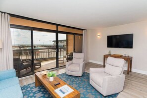 Une chambre d’hôtel moderne dotée d’un balcon, d’une télévision à écran plat et d’un coin salon comprenant deux fauteuils et un canapé.