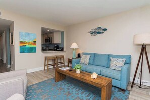 Een woonkamer met een blauwe bank, een houten salontafel en een blauw patroonloos vloerkleed.