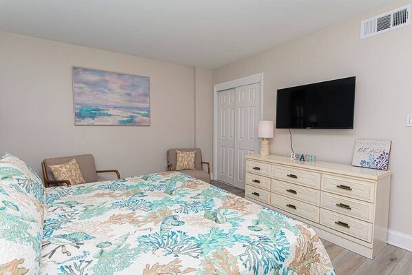 Une chambre à coucher comprenant un lit, deux chaises, une commode, un téléviseur et une porte.