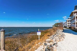 A coastal walkway with a sign, a rocky embankment, and a building with multiple balconies.
