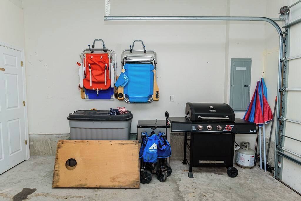 A garage with a grill, two wheeled luggage carts, a trash bin, and a wooden board.