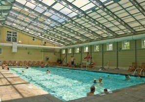 An indoor swimming pool with a glass ceiling, multiple lanes, and a diving board.