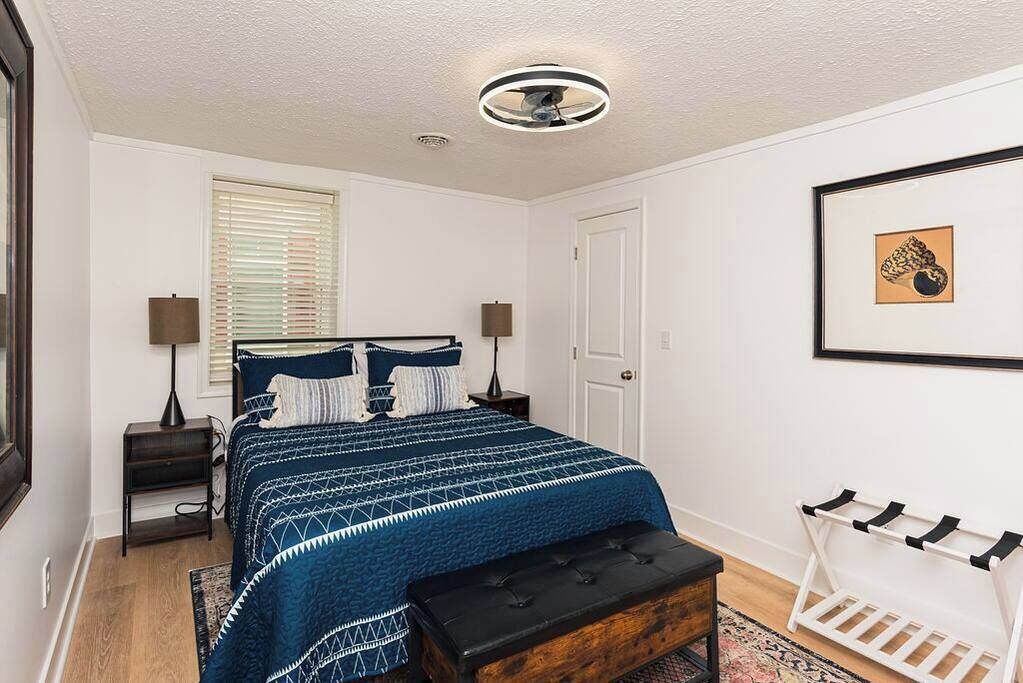 Une chambre à coucher comprenant un lit, des lampes de chevet, un banc, une étagère fixée au mur et un ventilateur de plafond.