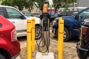 Ein Parkplatz mit Ladestationen für Elektrofahrzeuge, gekennzeichnet durch gelbe Poller, umgeben von abgestellten Autos.