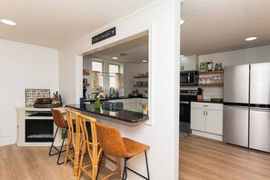 A modern kitchen with white cabinets, a black countertop, and a stainless steel refrigerator. There are two wooden chairs and a vase with flowers on the counter. - "The Hive"-Downtown Berlin, 4 BR, Sleeps 8, 2 Bath (Berlin)