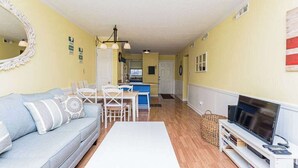 A living room with a sofa, a coffee table, a TV, and a dining area with chairs and a table. - Downtown Family Value - Sleeps 6 - with Pool (Ocean City)
