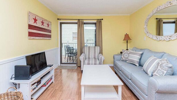 A living room with a sofa, a television on a stand, a coffee table, and a window with curtains. - Downtown Family Value - Sleeps 6 - with Pool (Ocean City)